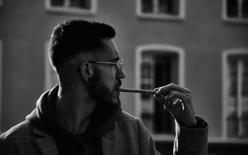 Ein Mann mit Brille und Bart im Freien. Er blickt gedankenverloren zur Seite und hält dabei einen Stift an den Mund.