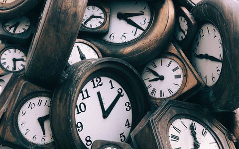 altertümliche analoge Uhren mit weißem Ziffernblatt und dunklem Holzrahmen, die auf einem Haufen liegen