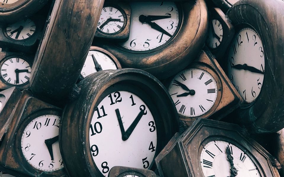 altertümliche analoge Uhren mit weißem Ziffernblatt und dunklem Holzrahmen, die auf einem Haufen liegen